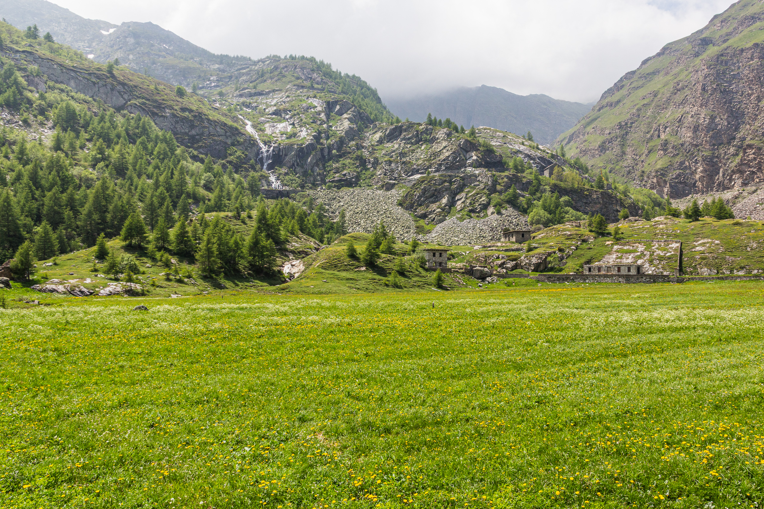 Almwiese mit Wasserfall und alten Steinhäusern